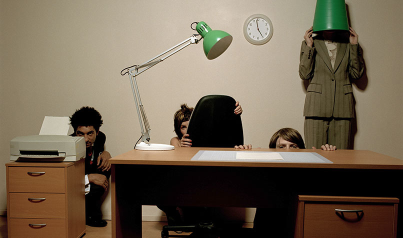 Business team hiding behind desk and lamp, avoiding accountability